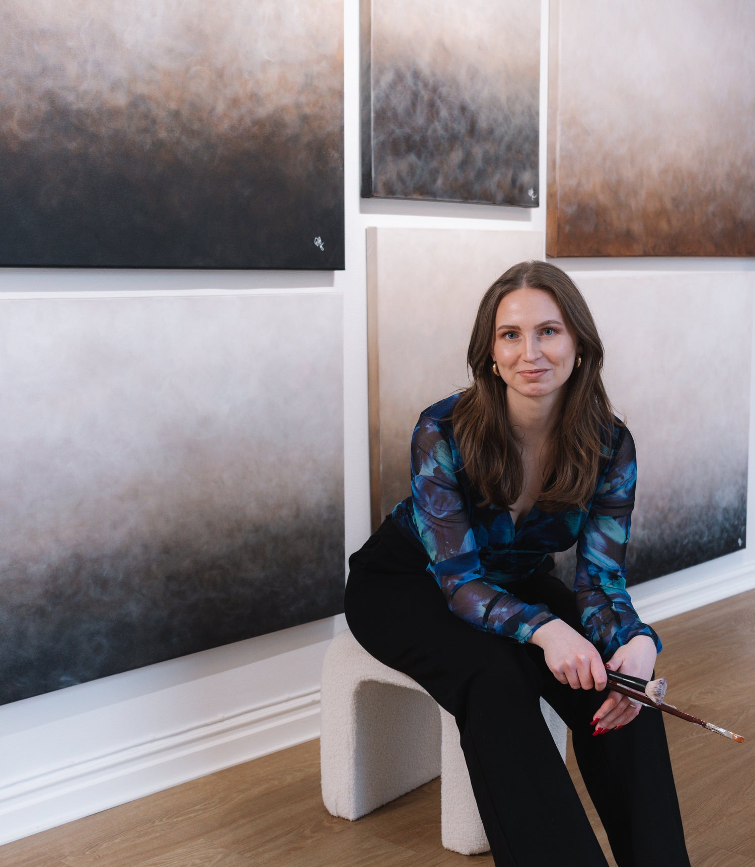 Konstnären Elin Palmgren som sitter på en pall framför sina abstrakta tavlor med gradienter